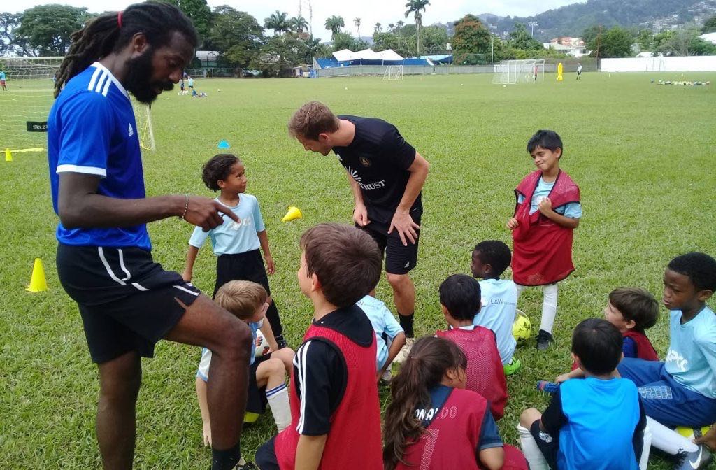 Coaches Yohance Marshall (L) and Matt Lawrey (C) speak with young players at the ATL FC training camp,St Mary’s grounds, in St Clair yesterday.