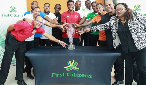Representatives of the 12 T&T Pro League clubs are flanked by Senior Manager Communication and public relations First Citizens Dexter Charles, second from right, and CEO Julia Baptiste, right, put their hands on the champions trophy during the Media Launch of the First Citizens Cup at the Diego Martin Sporting Complex, Bagatelle, Diego Martin, yesterday. ...CA-images