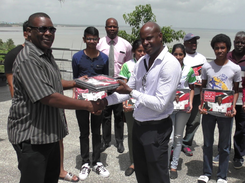 SSFL President William Wallace presents a copy of the Legacy of the Soca Warriors to St Benedict’s College head coach and former national player Leonson Lewis.