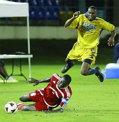 Economy Strikers captain Selwyn Isaacs, on the ground, puts in a sliding tackle on Marvin Jones of the Defence Force, in their bmobile National Super League Knockout semi-final at the Queen’s Park Oval, St Clair, yesterday.... Photo: Anthony Harris.
