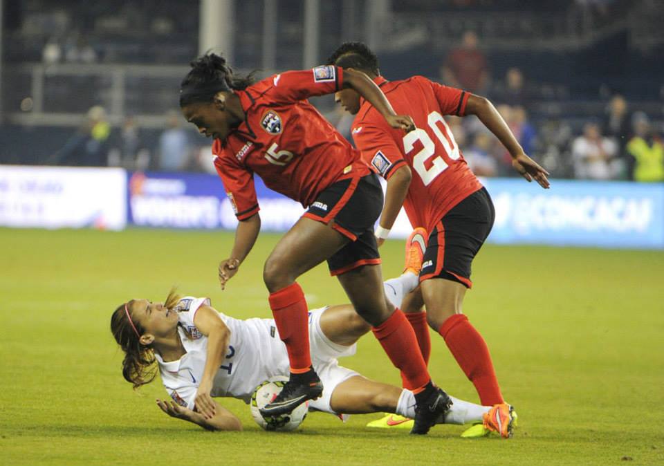 USA forward Alex Morgan (13) is knocked down by Trinidad & Tobago defender Liana Hinds (15) and midfielder Lauryn Hutchinson (20) in the first half during a women's World Cup qualifier soccer match at Sporting Park.