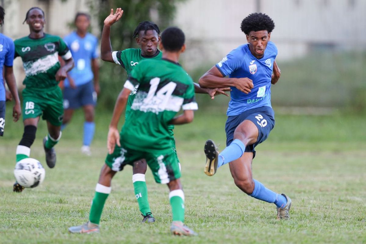 Naparima College striker Isreal Joseph, left, shoots and scores while under pressure from a St Augustine Secondary defender during the Secondary Schools Football League match at the St Augustine Secondary School yesterday, September 14th 2022 in St Augustine. Naparima College won 9-1. (Photo by Daniel Prentice)