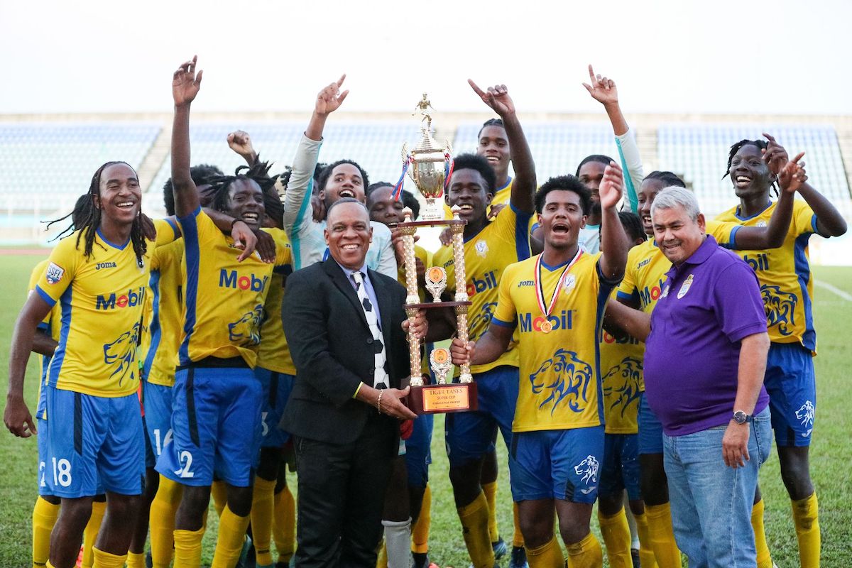 Caleb Boyce of Presentation College, centre, receives the winners’ trophy for the Tiger Tanks Cup from Secondary Schools Football League president Merere Gonzales, to his left, and Denis Latiff, Tiger Tanks Managing Director, to his right, while his teammates celebrate in the background after defeating Naparima College at the Ato Boldon Stadium in Couva, on Friday, September 9th 2022. Presentation won 3-2 in a penalty shootout after the scores were tied 1-1 at the end of regulation time. (Photo by Daniel Prentice)
