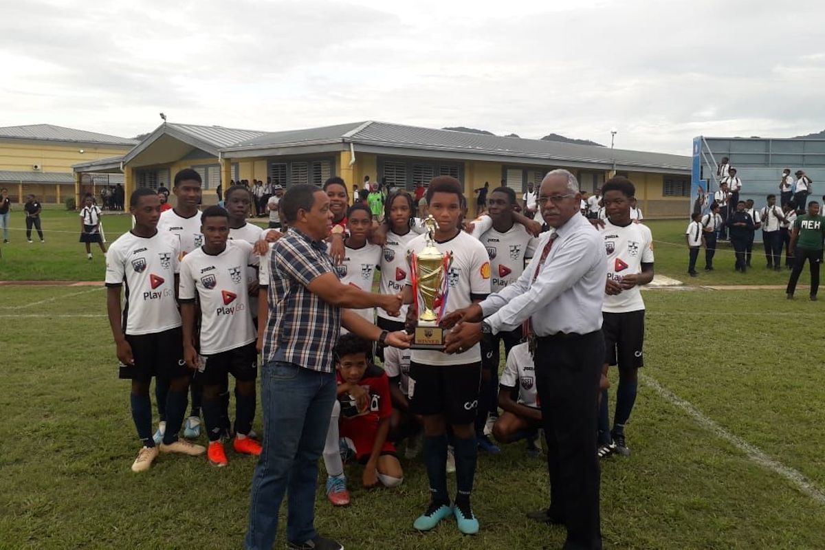In 2019, chairman of the East Zone in the Secondary Schools Football League Merere Louis Gonzales,  left, presents Trinity College East’s captain Nicholas Whiteman and its principal Derek West with the championship trophy after winning the Malta National Under-14 Division final at the college on Wednesday. Trinity defeated Scarborough Secondary 5-4 on penalty kicks after the scores were tied 2-2 at the end of regulation time. Khaden Caraby (25th) and Johnathan Emrith (55th) scored for Trinity and for Scarborough, Chris Waldron (17th) and Olando James (43rd) were the goal-scorers.