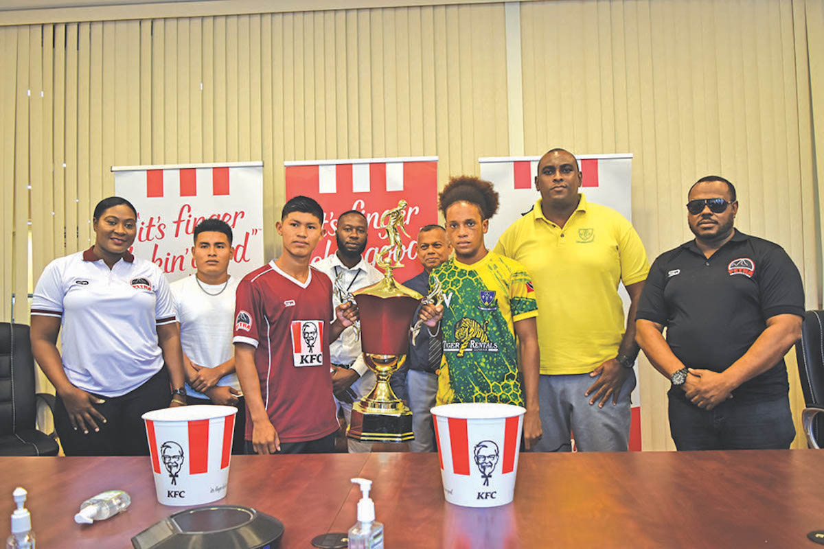 St. benedict’s and Waramadong’s captains get a hand on the trophy as they are flanked by KFC’s Kenneth Moonsammy and Esan Daniels, Coaches- Artherley Elliman and Nolan Bernard and Petra’s Jackie Boodie and Troy Mendonca